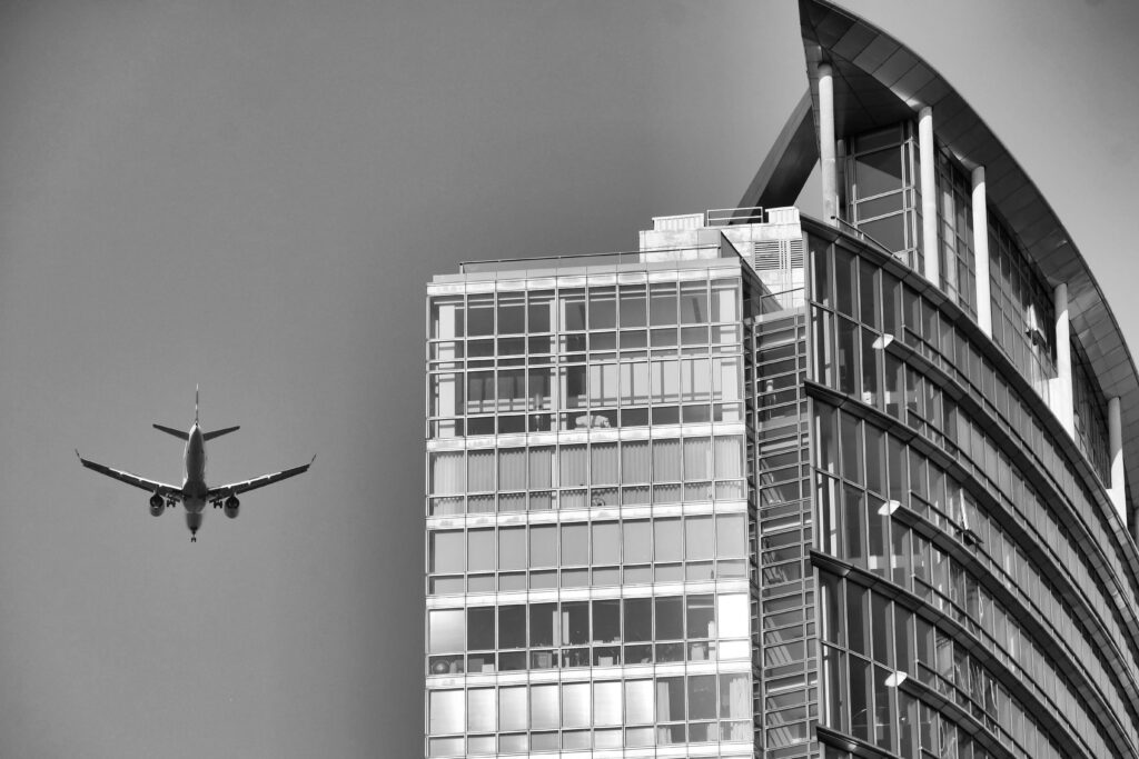 A black and white image showcasing an airplane flying near a modern skyscraper with glass facades.